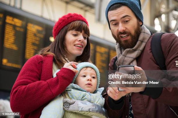 parents with child are looking at mobile phone in railway station. - betsie van der meer stock pictures, royalty-free photos & images