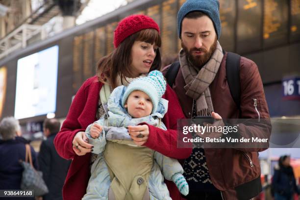 parents with baby are checking mobile phone while walking through railway station. - betsie van der meer stock pictures, royalty-free photos & images