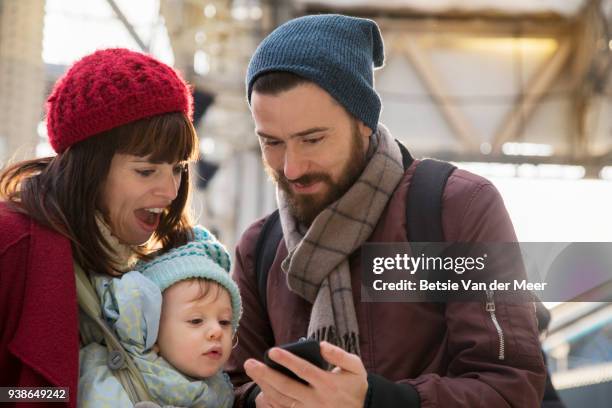 couple with child look at mobilephone in railroad station. - betsie van der meer stock pictures, royalty-free photos & images