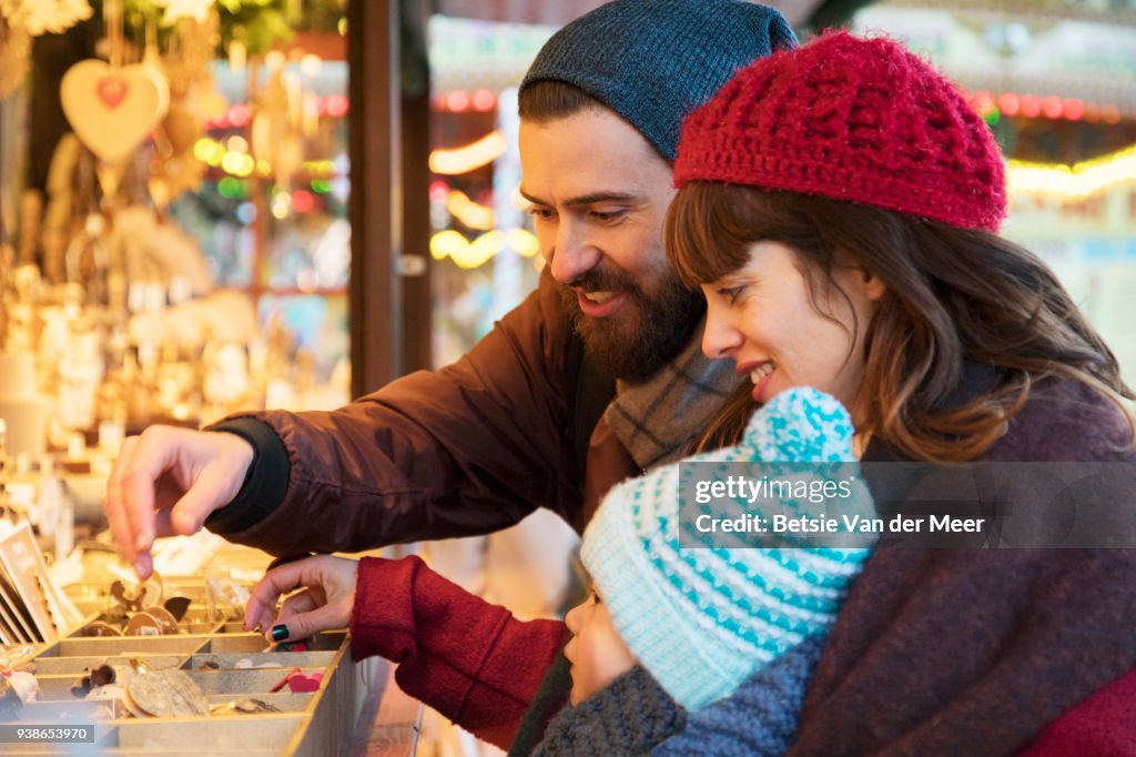 Parents show child ornaments at christmas stall.