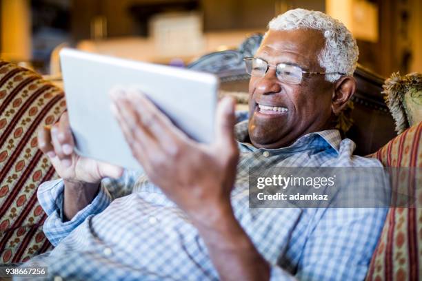 senior black man streaming on tablet - african american watching tv stock pictures, royalty-free photos & images