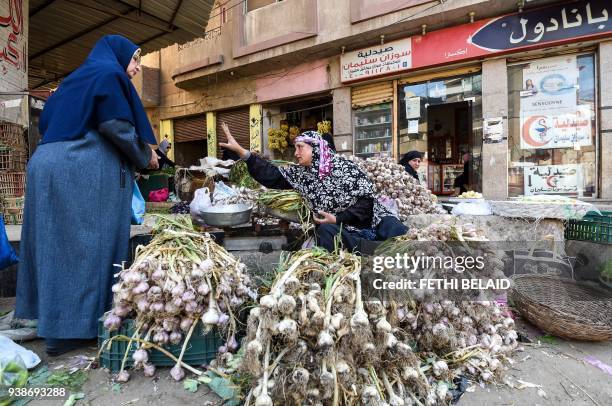 Picture taken on March 27, 2018 shows an Egyptian garlic peddlar haggling with a customer as she sits by her produce at a market in the Nile Delta...