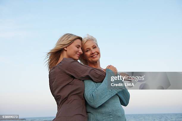 adult daughter hugging mother at beach - hija fotografías e imágenes de stock