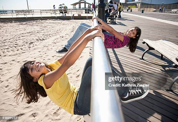 two young girls frolicking on boardwalk railing - coney island photos et images de collection