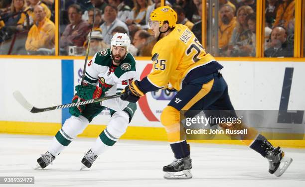 Daniel Winnik of the Minnesota Wild dumps the puck in the zone against Alexei Emelin of the Nashville Predators during an NHL game at Bridgestone...