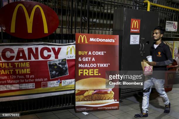 Courier of Swiggy, a food ordering and delivery service operated by Bundl Technologies Pvt., walks past menu items advertised outside a McDonald's...