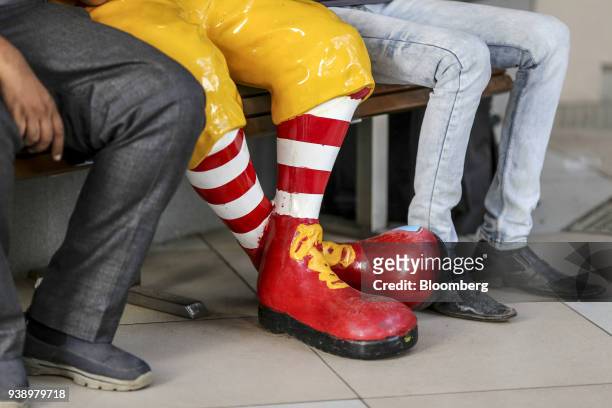 The legs and feet of food delivery couriers and a statue of Ronald McDonald are seen outside a McDonald's Corp. Restaurant, operated by Hardcastle...