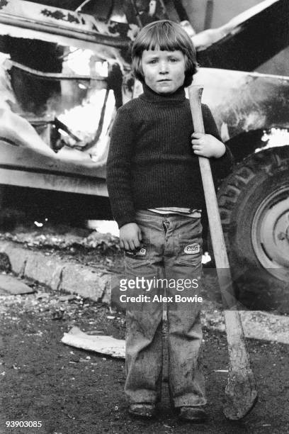 Young child with a hurley stick stands in front of a burning vehicle after hijacked vehicles were set on fire to celebrate the shooting of a British...