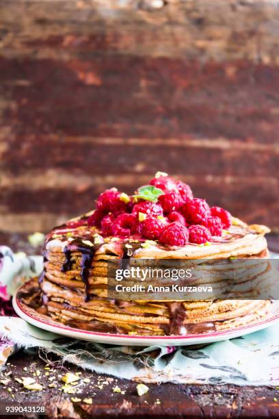 stack of wheat golden pancakes or pancake cake with freshly picked raspberry, chopped pistachios, chocolate sauce on a dessert plate, selective focus - raspberry sauce stock pictures, royalty-free photos & images