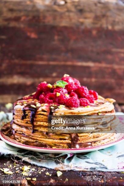 stack of wheat golden pancakes or pancake cake with freshly picked raspberry, chopped pistachios, chocolate sauce on a dessert plate, selective focus - raspberry sauce stock pictures, royalty-free photos & images