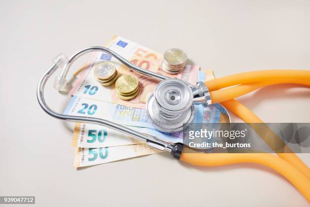 high angle view of euro banknotes and coins with stethoscope - medical insurance stock-fotos und bilder