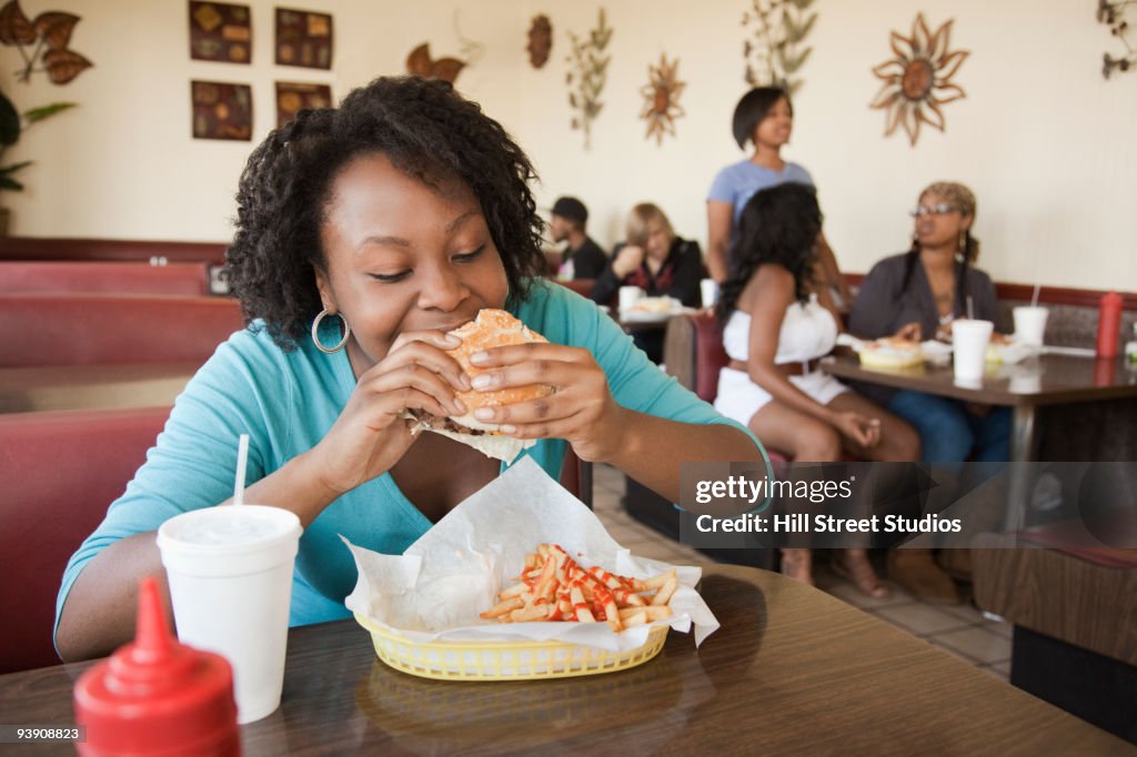 African woman eating hamburger in diner