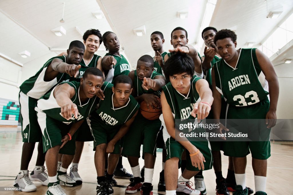 Basketball players pointing at camera in gym