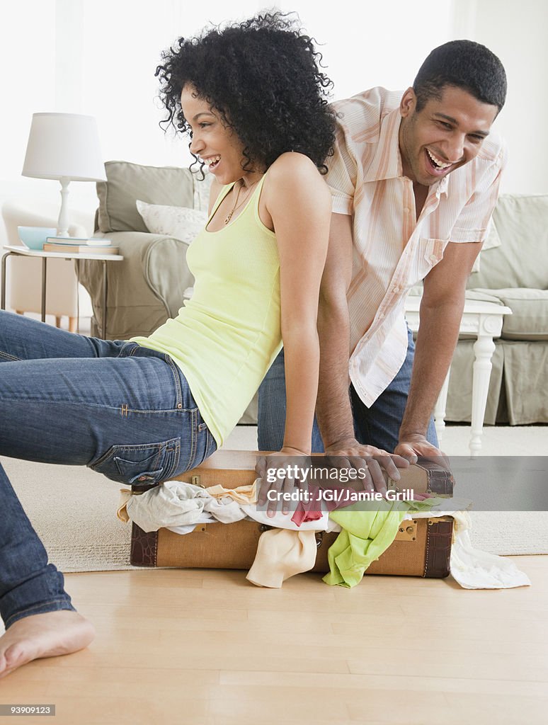 Couple stuffing clothes in small suitcase