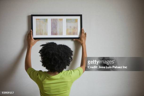 mixed race woman hanging picture on wall - hanging stock pictures, royalty-free photos & images