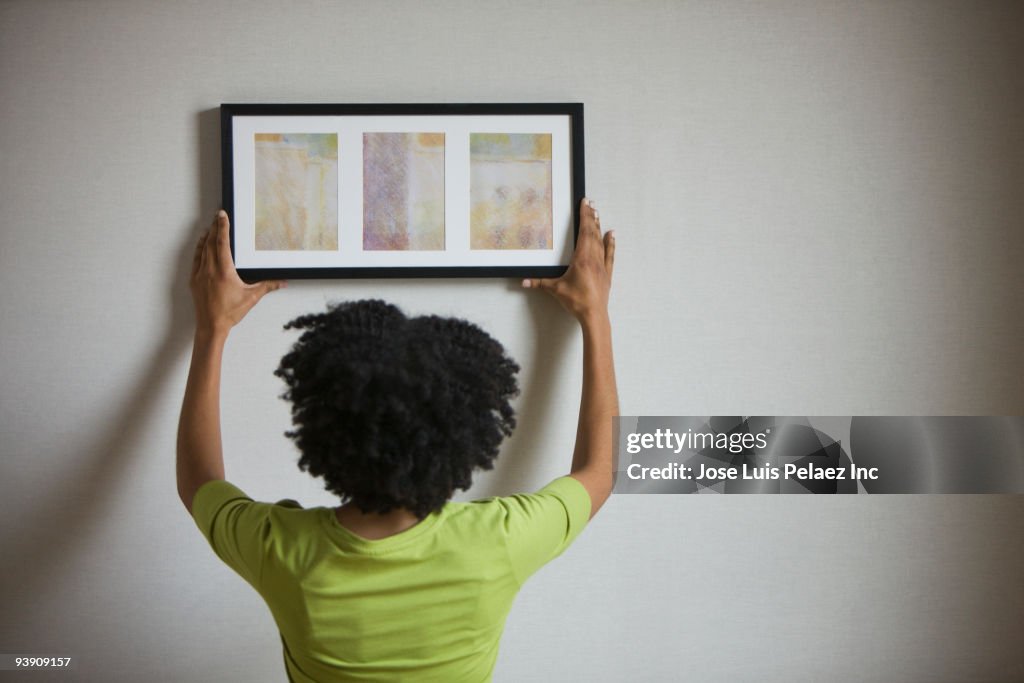 Mixed race woman hanging picture on wall