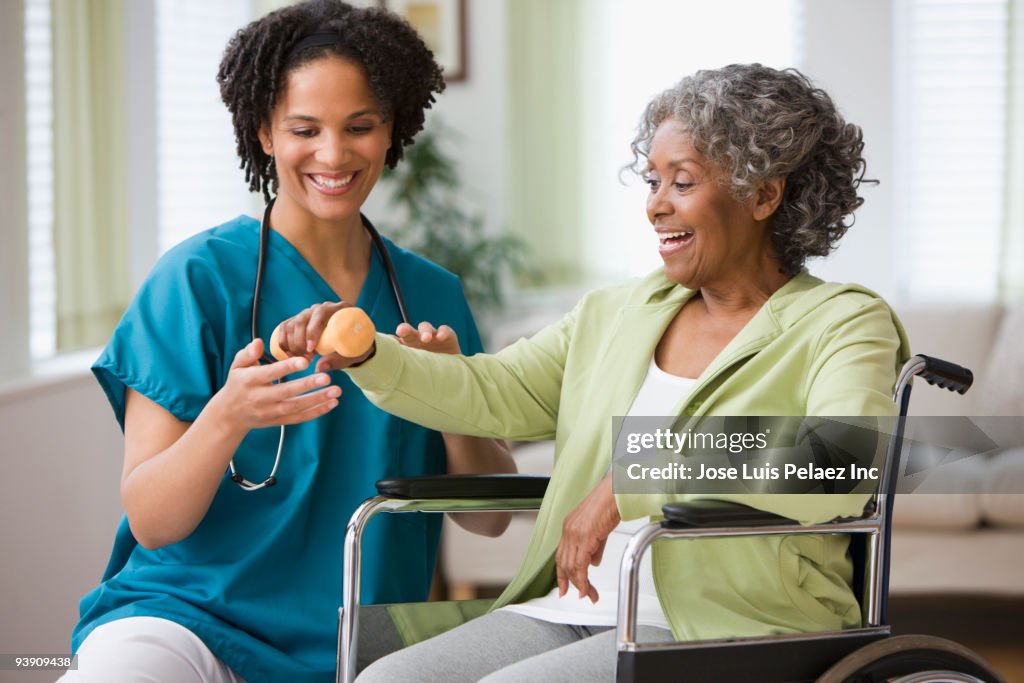 African home nurse helping woman in wheelchair with hand weight