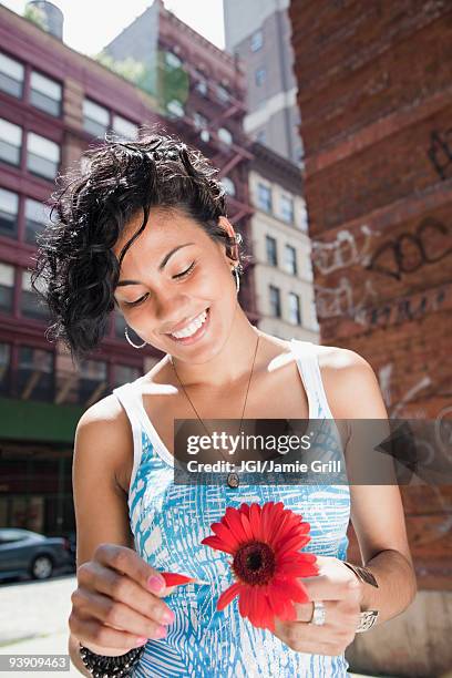 mixed race woman picking petals off flower on urban street - 花びら占い ストックフォトと画像