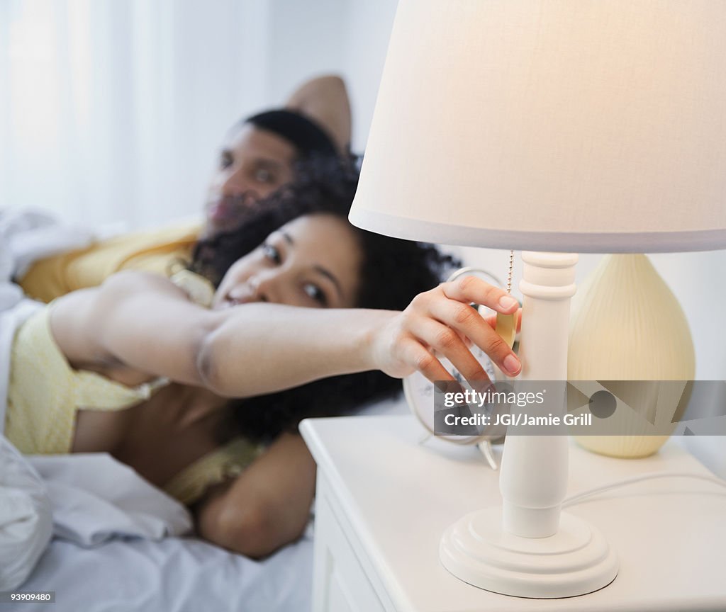 Woman in bed reaching to turn off bedside lamp