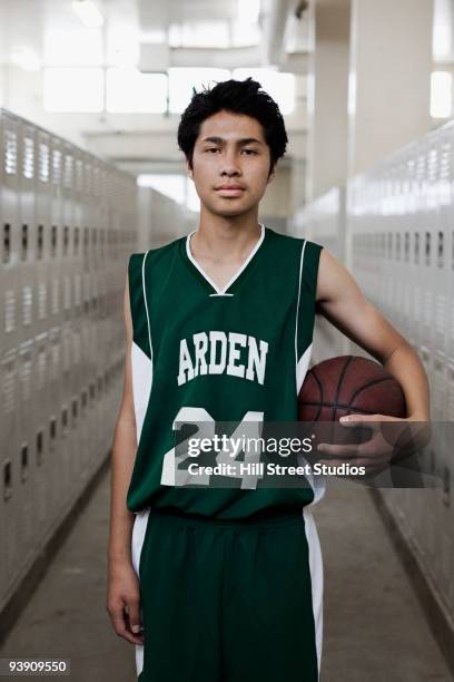 serious mixed race basketball player holding ball in locker room - basketball portrait stockfoto's en -beelden