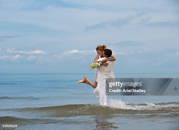 groom lifting bride in ocean surf - destination wedding imagens e fotografias de stock