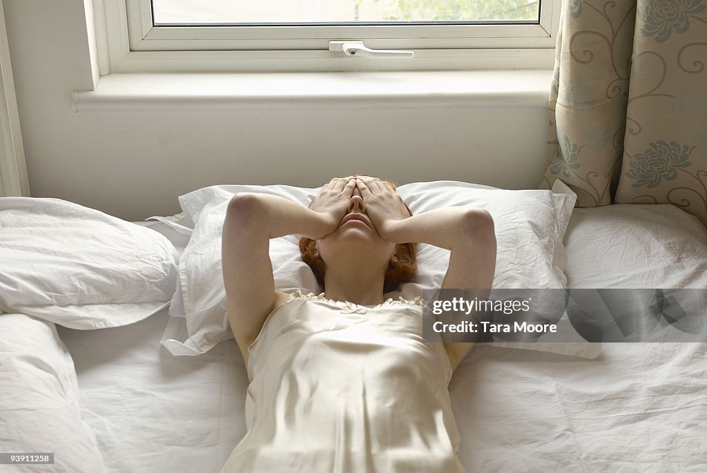 Woman on bed with hands over eyes