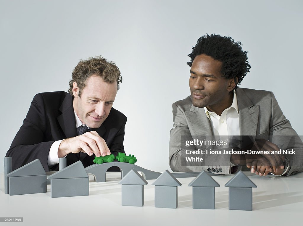 Two business men play with a train