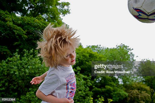 young boy heading a football. - ross woodhall stock-fotos und bilder