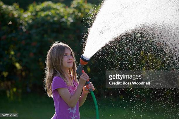 young girl spraying water with a hose - ross woodhall stock-fotos und bilder