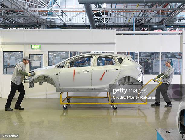 car plant workers moving shell of car - automobilbranche stock-fotos und bilder