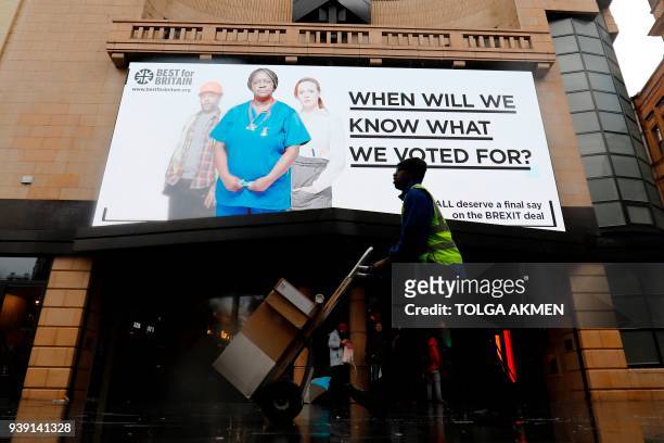 Pedestrians walk under a new billboard launched by campaign group Best for Britain in Leicester Square in London on March 28, 2018. Campaign group...