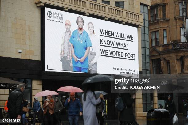 Pedestrians walk under a new billboard launched by campaign group Best for Britain in Leicester Square in London on March 28, 2018. Campaign group...