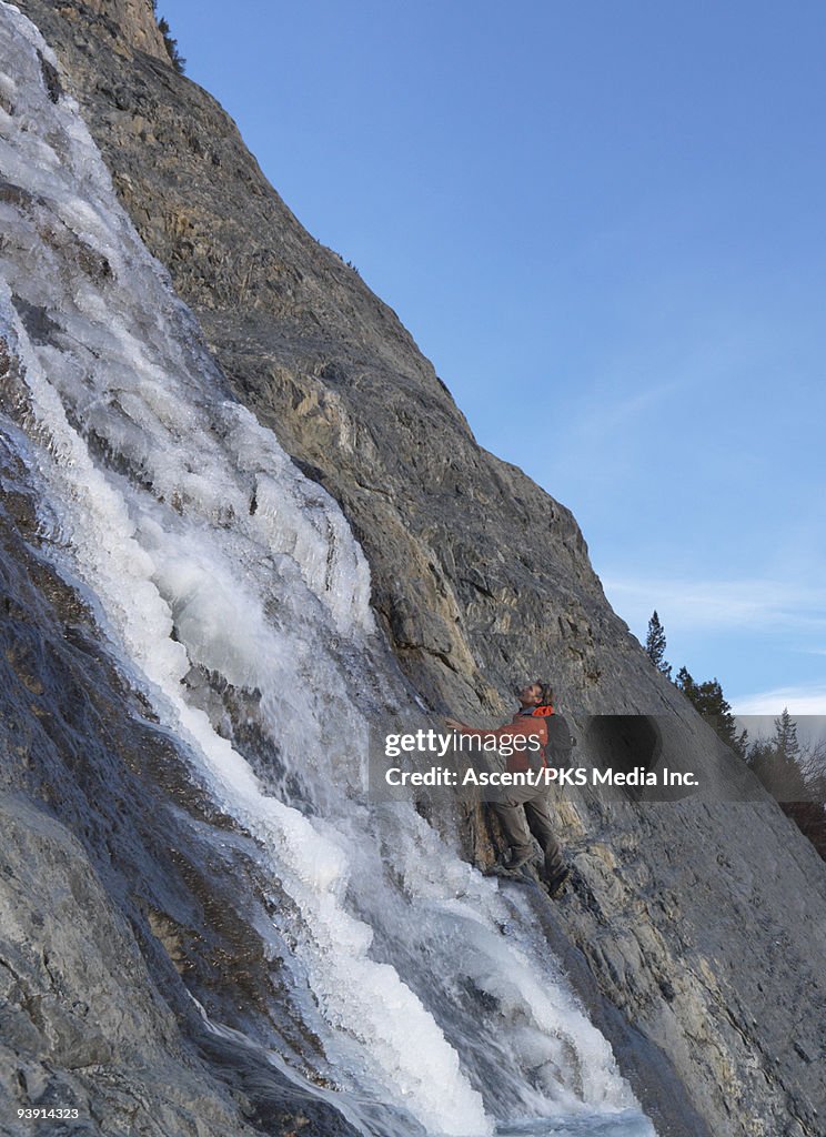 Mountaineer climbs rock alongside frozen waterfall