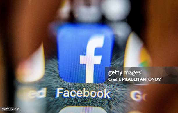 An illustration picture taken through a magnifying glass on March 28, 2018 in Moscow shows the icon for the social networking app Facebook on a smart...