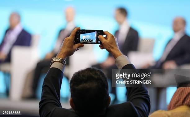 Man uses a cell phone to take pictures of speakers seated on the podium during the Iraq Energy Forum in the capital Baghdad on March 28, 2018. / AFP...