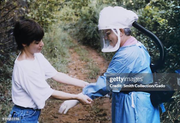 Two Centers for Disease Control health officials preparing containment suit for a Hantavirus field study, 2004. Image courtesy Centers for Disease...