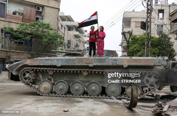 Syrian children hold a national flag while standing atop an infantry fighting vehicle in the Eastern Ghouta town of Hazzeh on the outskirts of the...