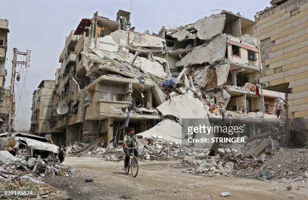Syrian man rides a bicycle past a destroyed building in the town of Hazzeh in Eastern Ghouta, on the outskirts of the Syrian capital Damascus, on...