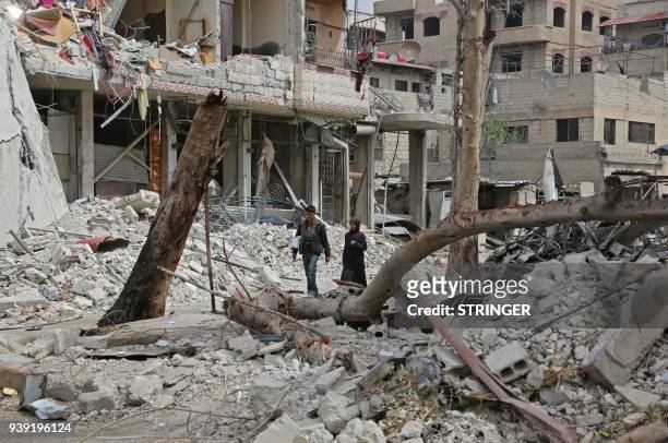 Syrians walk past a destroyed building in the town of Hazzeh in Eastern Ghouta, on the outskirts of the Syrian capital Damascus, on March 28, 2018.