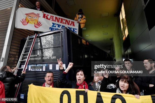 Protesters opposing properties auctions hold a banner atop a police bus blocking access to a public notary's office in Athens on March 28, 2018....