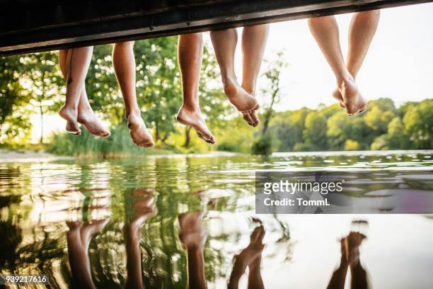 grupo de amigos piernas balanceándose de embarcadero - leisure activity fotografías e imágenes de stock