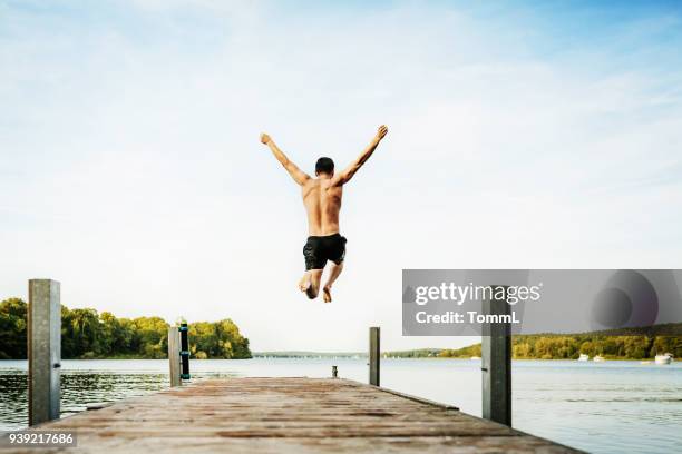 ung kille hoppar av brygga vid sjön - jumping bildbanksfoton och bilder