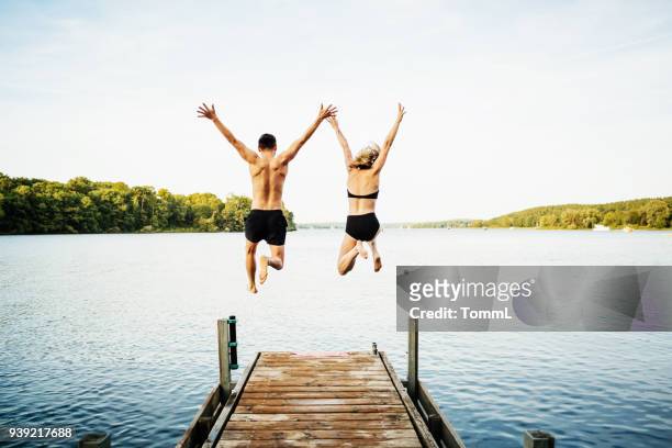 two friends jumping off jetty at lake together - lake stock pictures, royalty-free photos & images