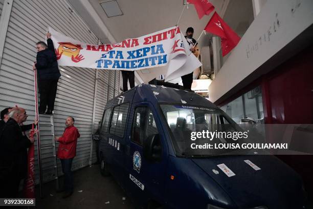 Protesters opposing property auctions hold a banner atop a police van blocking their access to a public notary's office in Athens on March 28, 2018...