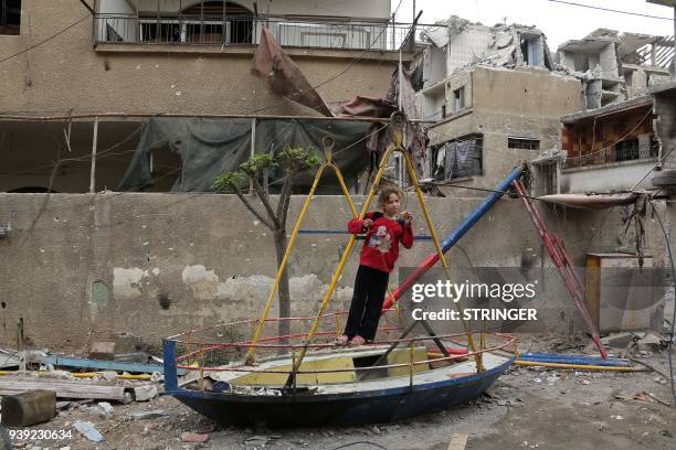 Picture taken on March 28, 2018 shows a Syrian child playing on a damaged toy in the town of Hazzeh in Eastern Ghouta, on the outskirts of the Syrian...