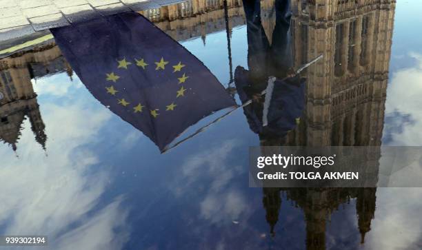 An anti-Brexit demonstrator is reflected in a rainwater puddle as he waves a European Union flag outside the Houses of Parliament in London on March...