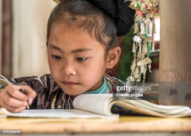 Concentrated Learner School, writing. looking away, selective focus, small Dong Village, Huang Gang."nChild is dressed in traditional Dong clothing.The Dong is a minority people in China.