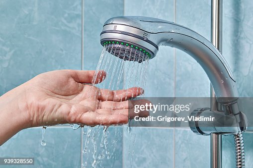 Flexible hose shower clamped to holder, hand checks water temperature. Flexible hose shower clamped to holder, hand checks water temperature.