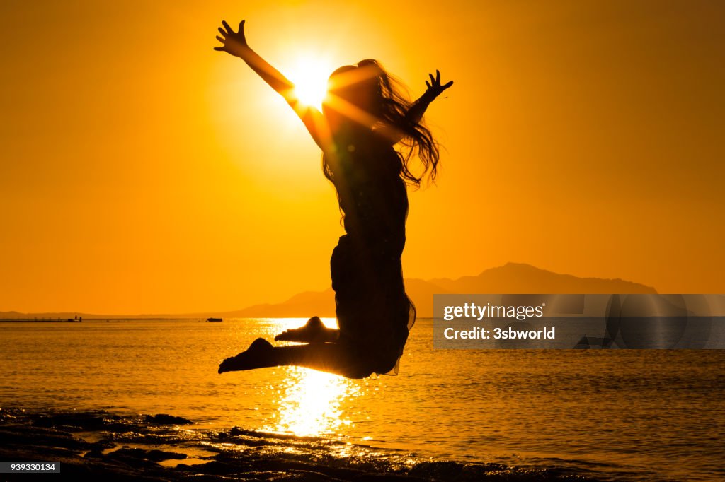 Silhouette of girl jumping against sunrise