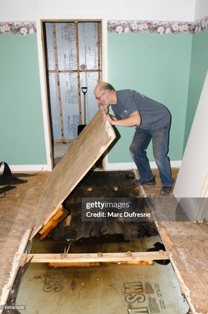 Mannen att ta bort träskiva från golvet efter skador i källaren som orsakats av avlopp återflödet beror på igensatta sanitära avlopp